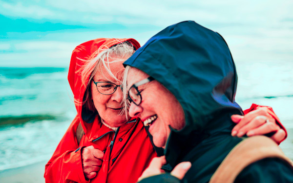 People in raincoats on a beach hugging and laughing