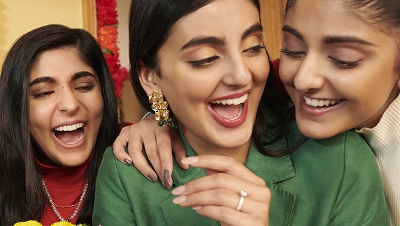 A woman showing off her engagement ring to two girls.