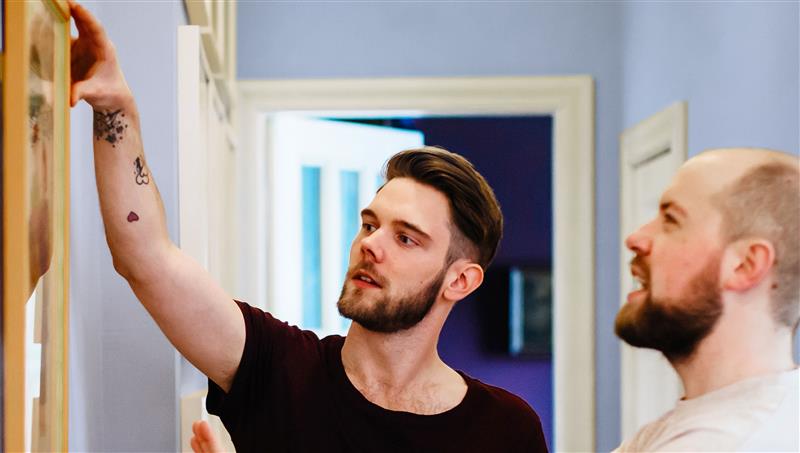 Two men fixing an item onto a wall.