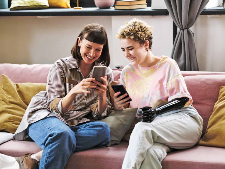 Two people sat laughing whilst looking at their mobile phones.