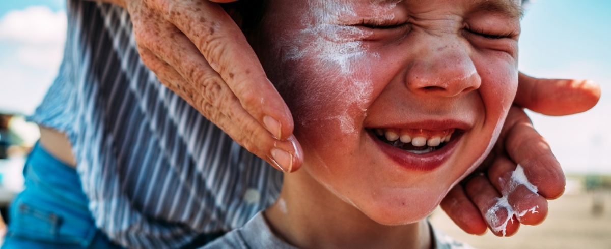 Smiling young boy having sun cream applied.